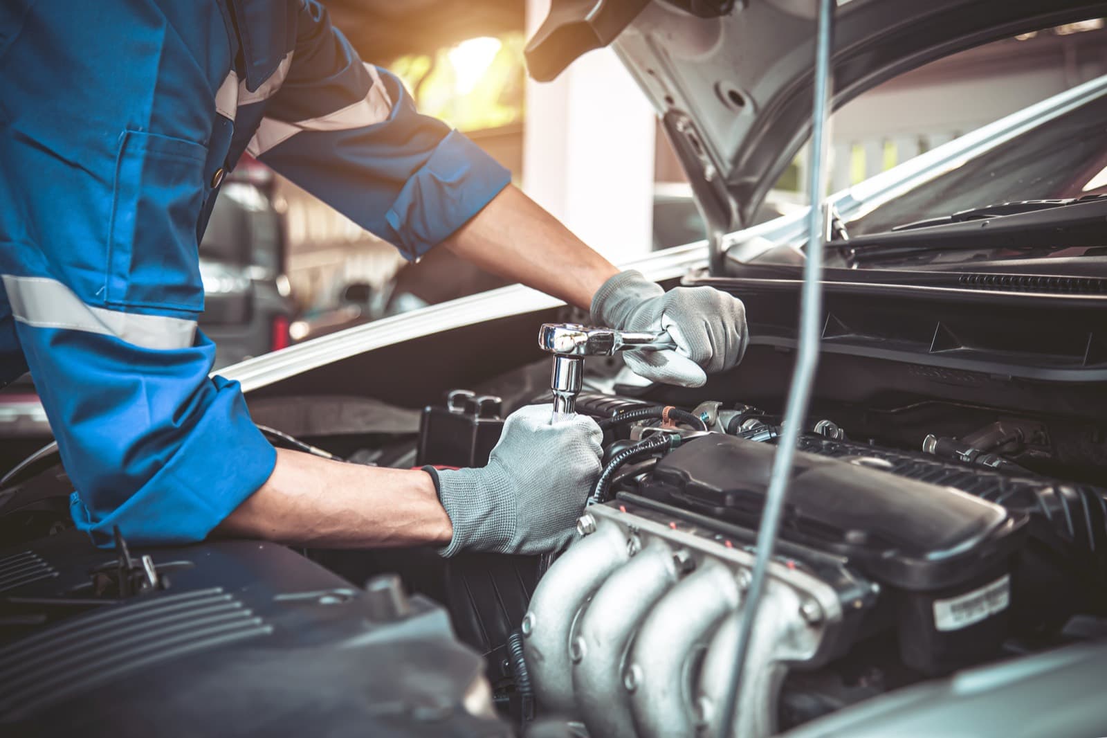 A technician in work gloves uses a ratchet under the open hood of a vehicle.