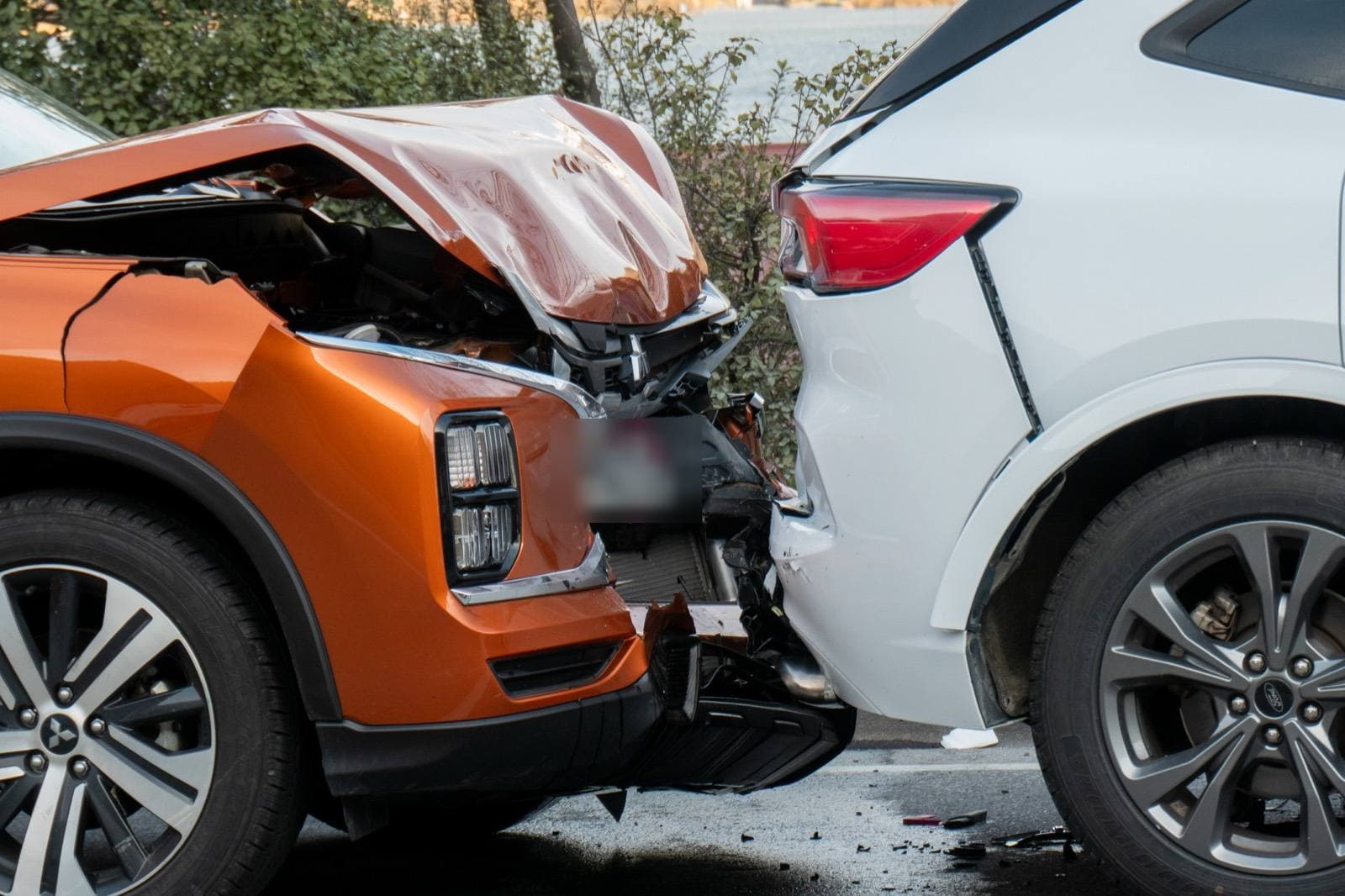 Two SUVs after a collision, the orange one with heavy front-end damage against the rear of a white SUV.
