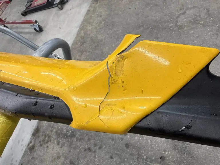 A yellow bumper cover with a visible crack and scraped paint rests on a padded stand.
